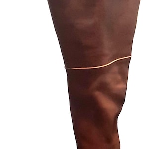 Op de afbeelding: Een hoge, bruine leren laars met een vierkante neus en een dunne, goudkleurige band rond de bovenkuit. De laars is gemaakt van glad leer en heeft een klassiek, op paardensport geïnspireerd ontwerp.