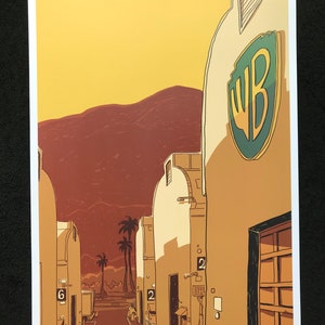 Puede incluir: Una ilustración digital de una calle bordeada de edificios, con un gran logotipo de Warner Bros. en el edificio de la derecha. Los edificios son de color amarillo pálido con techos de tejas rojas. La calle está bordeada de palmeras y el fondo es una puesta de sol.