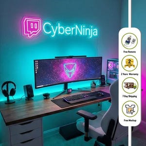 May include: A custom neon sign mounted on a wall displaying the text CyberNinja in a bright pink and cyan glow. The sign features a stylized speech bubble icon next to the text, illuminating a desk setup with a wide monitor and keyboard.