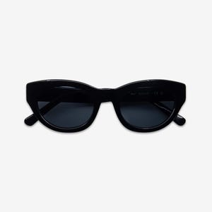 May include: Black cat-eye sunglasses with dark lenses. The sunglasses have a thick, rounded frame and a subtle upward curve at the outer edges. The lenses are a dark, solid color, providing a sleek and stylish look. The sunglasses are set against a plain white background.