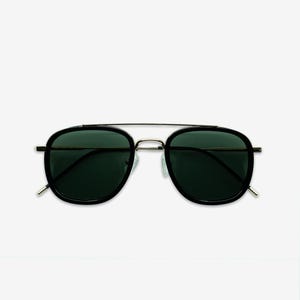 May include: Black sunglasses with a gold-colored metal bridge and temples. The lenses are dark green, and the frames are black. The sunglasses have a classic aviator style.