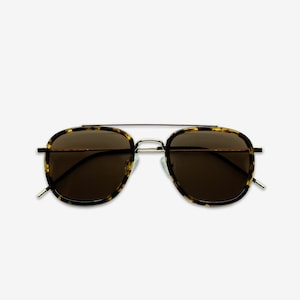 May include: Aviator-style sunglasses with a gold-colored metal frame and dark brown lenses. The frames have a tortoiseshell pattern. The sunglasses have a double bridge and a classic, timeless design.
