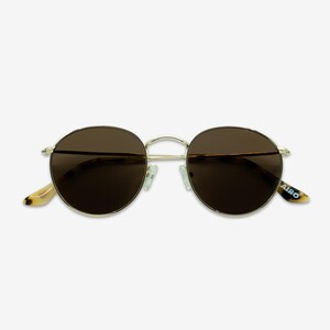 May include: Round sunglasses with a gold metal frame and brown lenses. The temples have a tortoiseshell pattern and the brand name "AIRO" is printed on the right temple. The sunglasses are designed for eye protection.