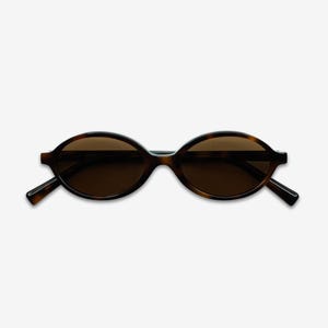 May include: Oval-shaped sunglasses with a dark brown tortoiseshell frame and tinted lenses. The sunglasses have a classic design with a slightly rounded shape, suitable for various face shapes. The arms are thin and extend to the temples.