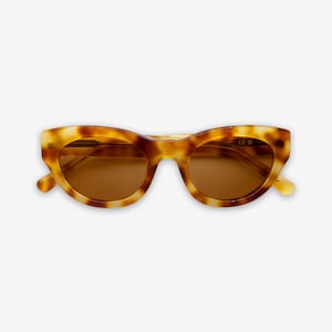 May include: Tortoiseshell-patterned sunglasses with brown lenses. The cat-eye frames have a rounded shape and a light brown and yellow color scheme. The sunglasses are set against a white background.