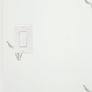 May include: A white light switch with a single toggle switch on a white wall with a black and white bull skull design wallpaper.