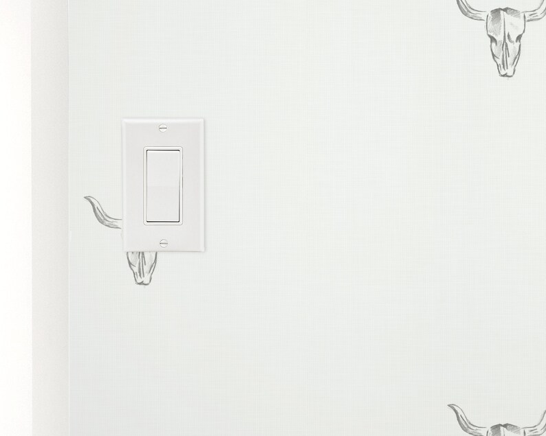 May include: A white light switch with a single toggle switch on a white wall with a black and white bull skull design wallpaper.