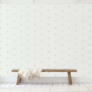 May include: A white wall with a repeating pattern of gray deer heads. A wooden bench with a white blanket sits in front of the wall.