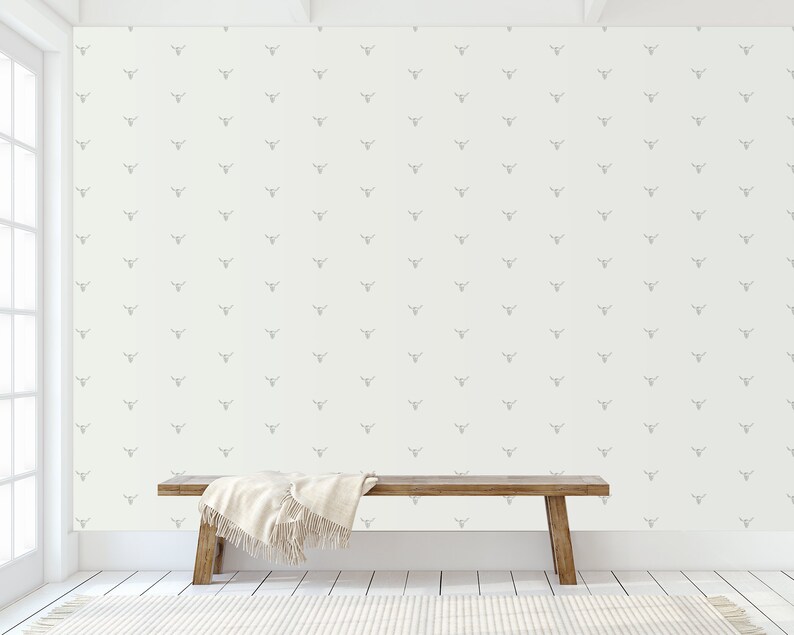 May include: A white wall with a repeating pattern of gray deer heads. A wooden bench with a white blanket sits in front of the wall.