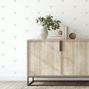 May include: A light wood cabinet with two doors and black metal legs. The cabinet is decorated with a vase of green plants and a stack of books. The wall behind the cabinet is white and has a pattern of small, gray bull skulls.