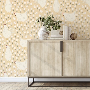 May include: A beige wallpaper with a repeating pattern of white chickens and small white flowers. A wooden cabinet with two doors sits in front of the wallpaper. The cabinet has a light wood finish and black metal legs.