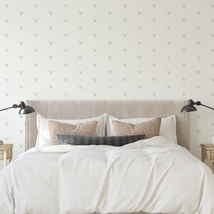 May include: A white bedroom with a beige headboard and white bedding. The walls are covered in a white wallpaper with a repeating pattern of small grey animal heads.