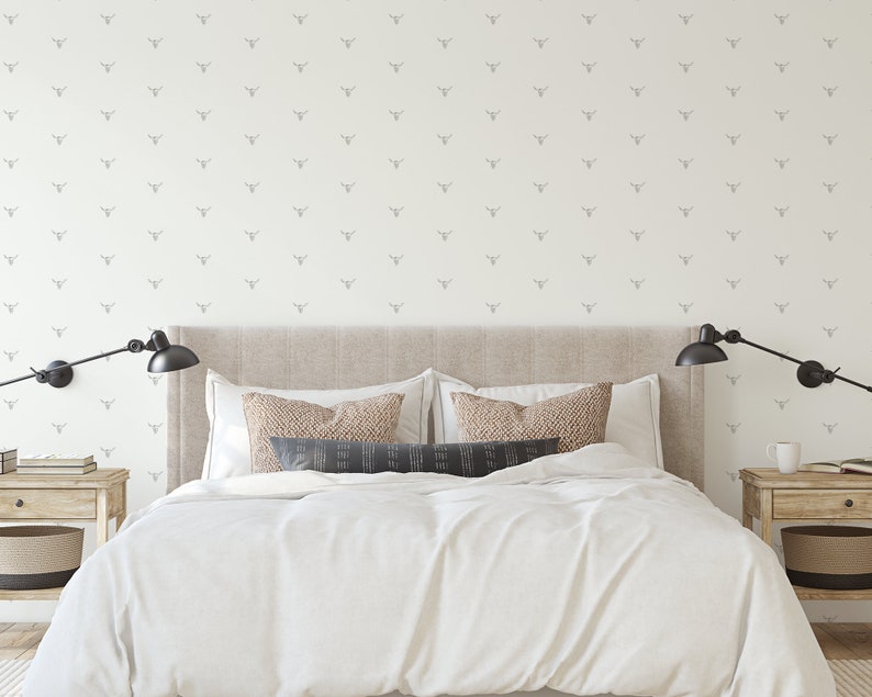 May include: A white bedroom with a beige headboard and white bedding. The walls are covered in a white wallpaper with a repeating pattern of small grey animal heads.