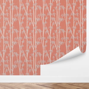 May include: A coral pink wallpaper with a white bamboo pattern. The wallpaper is shown on a wall with a white baseboard and a wood floor.