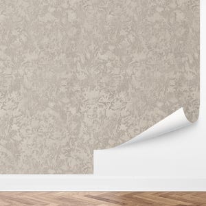 May include: Textured wallpaper in neutral tones, featuring an abstract design. A section of the wallpaper is affixed to a white wall, with a rolled edge showing the white backing. The wall meets a wooden floor.