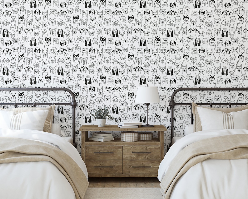 Pode incluir: Duas camas de solteiro com roupa de cama branca e cobertores bege em um quarto com paredes brancas e papel de parede com rostos de c&atilde;es em preto e branco. Uma mesa de cabeceira de madeira com uma l&acirc;mpada e livros fica entre as camas.