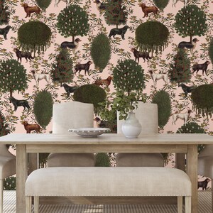 May include: A dining room table set with two chairs and a bench, all upholstered in a cream fabric. The table is made of wood and has a light brown finish. The background is a pink wallpaper with a repeating pattern of dogs, trees, and flowers.