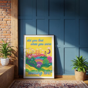 May include: A framed art print with a yellow background and a colorful landscape illustration. The artwork features a bridge, mountains, trees, and a rainbow. Text at the top reads "did you find what you were" and at the bottom "looking for?"