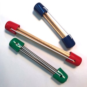 Puede incluir: Tres juegos de agujas de tejer en estuches protectores. Las agujas son de madera y metal. Los estuches son azul, rojo y verde.