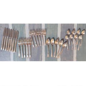 May include: A collection of vintage silverware, including knives, forks, and spoons, arranged on a striped surface. The silverware has ornate detailing and a shiny, metallic finish. The arrangement suggests a formal dining setting.