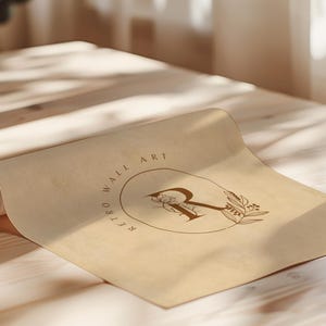 May include: A rolled-up sheet of tan paper with the words "RETRO WALL ART" encircling a floral design and the letter "R". The paper is lying on a light-colored wooden surface.