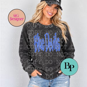 May include: A charcoal grey acid-wash long-sleeve sweatshirt featuring the text Blue Devils in a bright blue font with a white outline. The garment has a crew neckline and raglan sleeves, providing a relaxed fit for casual wear.