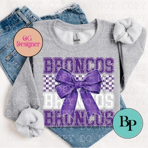 Puede incluir: Una sudadera gris jaspeado de cuello redondo con la palabra BRONCOS impresa en letras mayúsculas moradas con bordes blancos, sobre un patrón de cuadros morados, centrada con un gráfico de un lazo morado grande en el frente.