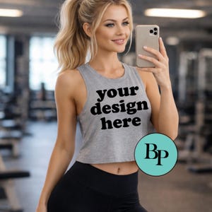 May include: Gray crop top with the text "your design here" in black. The top is sleeveless and worn with black leggings. A teal circle with the letters "Bp" is in the lower right corner.