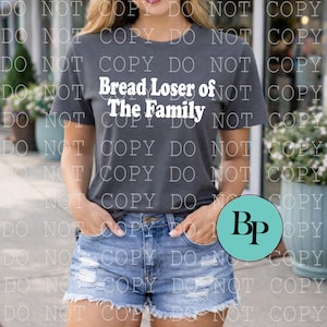 May include: Dark gray t-shirt with the text "Bread Loser of The Family" in white. The shirt is paired with denim shorts. The image includes a teal circle with the letters "Bp".