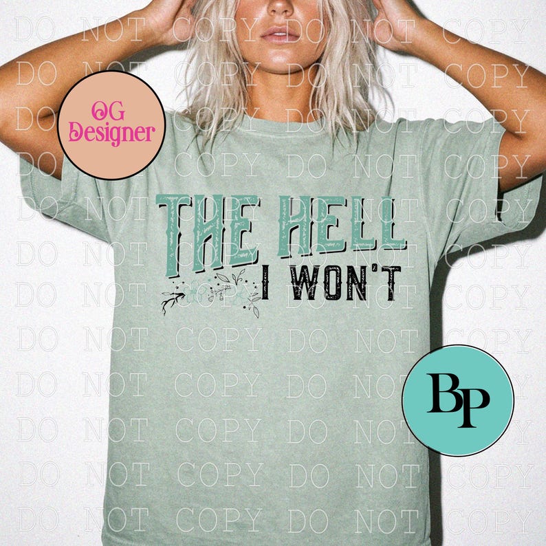 May include: A sage green short-sleeve t-shirt featuring the text THE HELL I WON'T printed in a distressed black and teal font. The design includes small floral line art accents below the text, set against a solid, muted green fabric background.