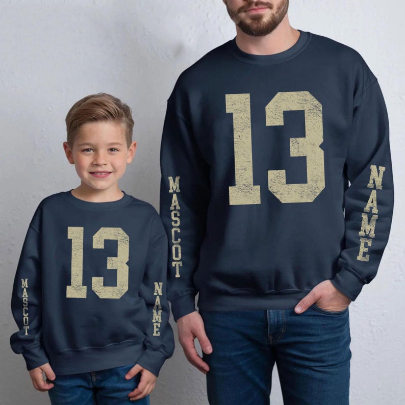 A young boy and an adult wearing matching navy blue sweatshirts with the number 13 and the word "Mascot" printed on them.
