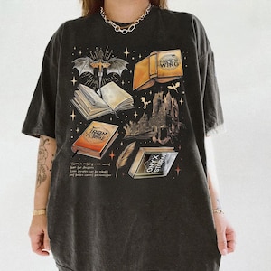 a person wearing a black t-shirt with a graphic design depicting various books and symbols, including a bat, castle, and lightning bolt.