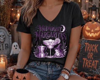 Può includere: Una t-shirt nera con scollo a V caratterizzata da una stampa grafica viola con il testo Midnight Margaritas, un bicchiere da cocktail, una moka, una luna crescente e una rana con cappello da strega sul davanti della maglia a maniche corte.