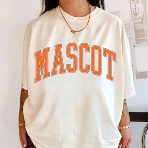 A person wearing a white t-shirt with the word "MASCOT" printed in orange letters.