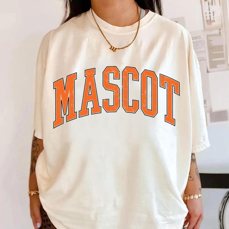A person wearing a white t-shirt with the word "MASCOT" printed in orange letters.