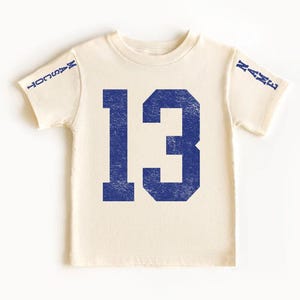 A white t-shirt with the number 13 printed in blue.