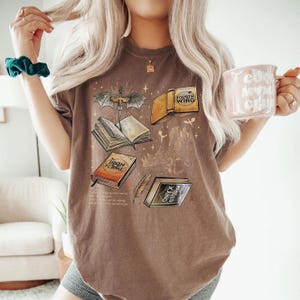 A woman with long blonde hair is wearing a brown t-shirt with a graphic design featuring books and a mug.