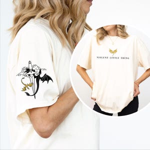 May include: A white ceramic mug with a black handle and the text "But First, Coffee" in a bold, black font. The mug is set against a blurred background, suggesting a cozy setting.