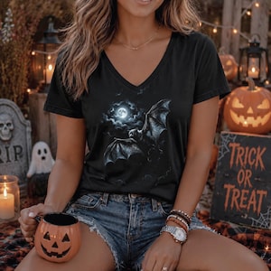 May include: A black V-neck t-shirt featuring a graphic print of a bat flying in front of a full moon surrounded by clouds. The shirt has short sleeves and a straight hemline, constructed from a solid black fabric with a detailed nocturnal scene.