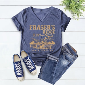 a casual outfit consisting of a blue t-shirt with a graphic design, blue sneakers, and blue jeans laid out on a white background.