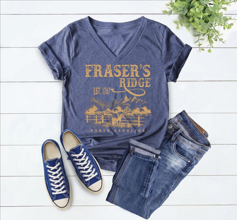 a casual outfit consisting of a blue t-shirt with a graphic design, blue sneakers, and blue jeans laid out on a white background.