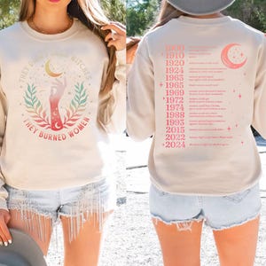 a woman wearing a white sweatshirt with a graphic design on the front and a list of years on the back.