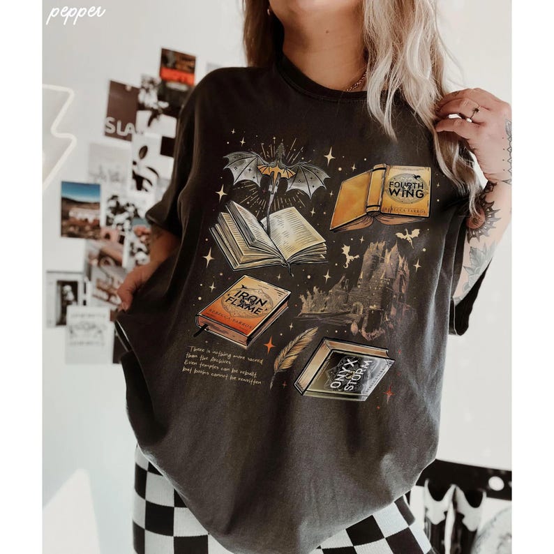 A person wearing a black t-shirt with a graphic design featuring various books and a bat, along with some text.