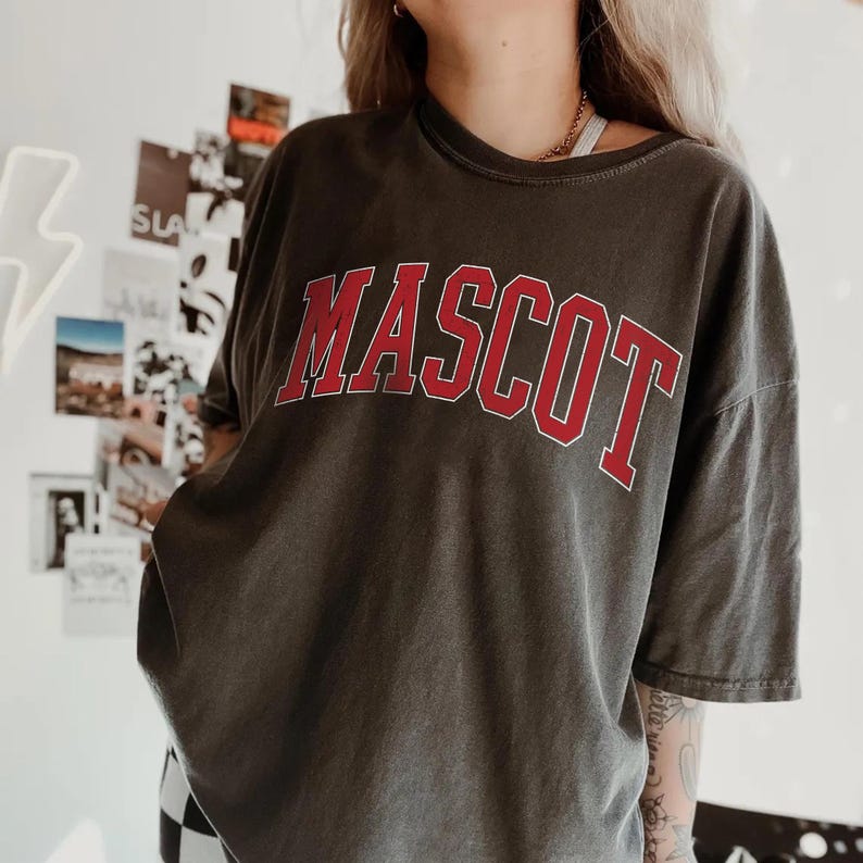 A person wearing a grey t-shirt with the word "MASCOT" printed on it.