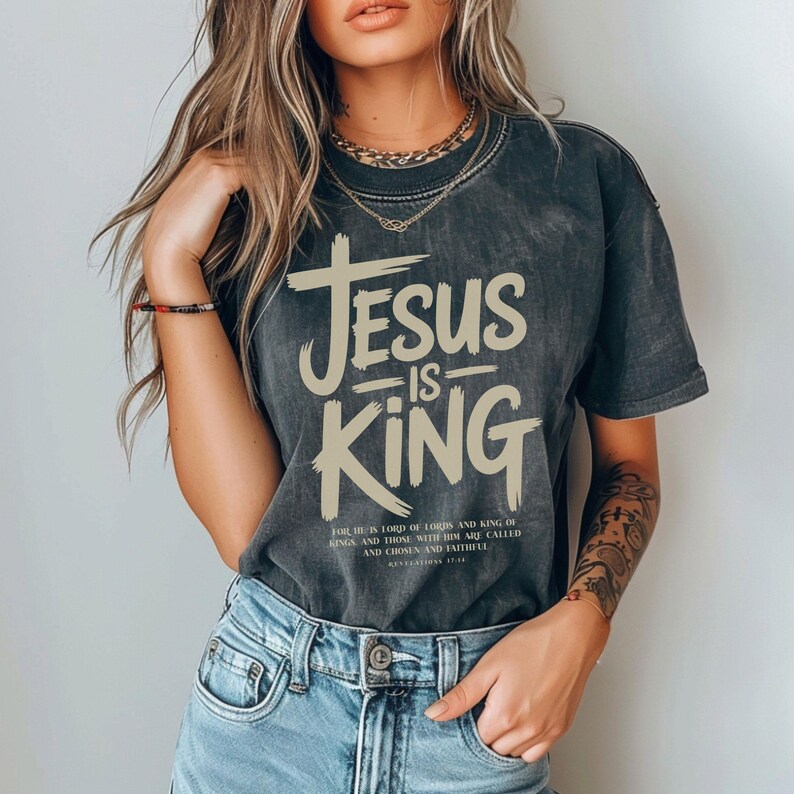 A woman wearing a black t-shirt with the text "JESUS IS KING" printed on it, standing against a white background.