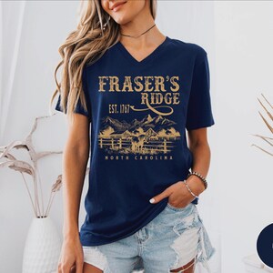 A woman wearing a navy blue t-shirt with a graphic design of a mountain range and the text "Fraser's Ridge" printed on it.
