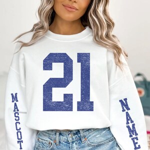 A woman wearing a white sweatshirt with the number 21 and the word "Mascot" printed on it.