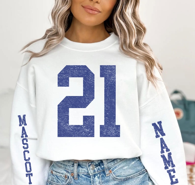 A woman wearing a white sweatshirt with the number 21 and the word "Mascot" printed on it.