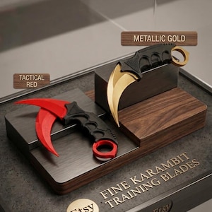Pode incluir: Duas lâminas de treino karambit com cabos pretos e lâminas curvas em dourado metálico e vermelho tático. As lâminas estão expostas num suporte de madeira escalonado com etiquetas TACTICAL RED e METALLIC GOLD, e o texto FINE KARAMBIT TRAINING BLADES.