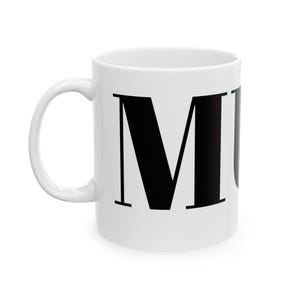 May include: White ceramic mug featuring a large black letter "M". The mug has a curved handle and a simple design. Suitable for hot or cold drinks. The mug is a standard size for a hot beverage.